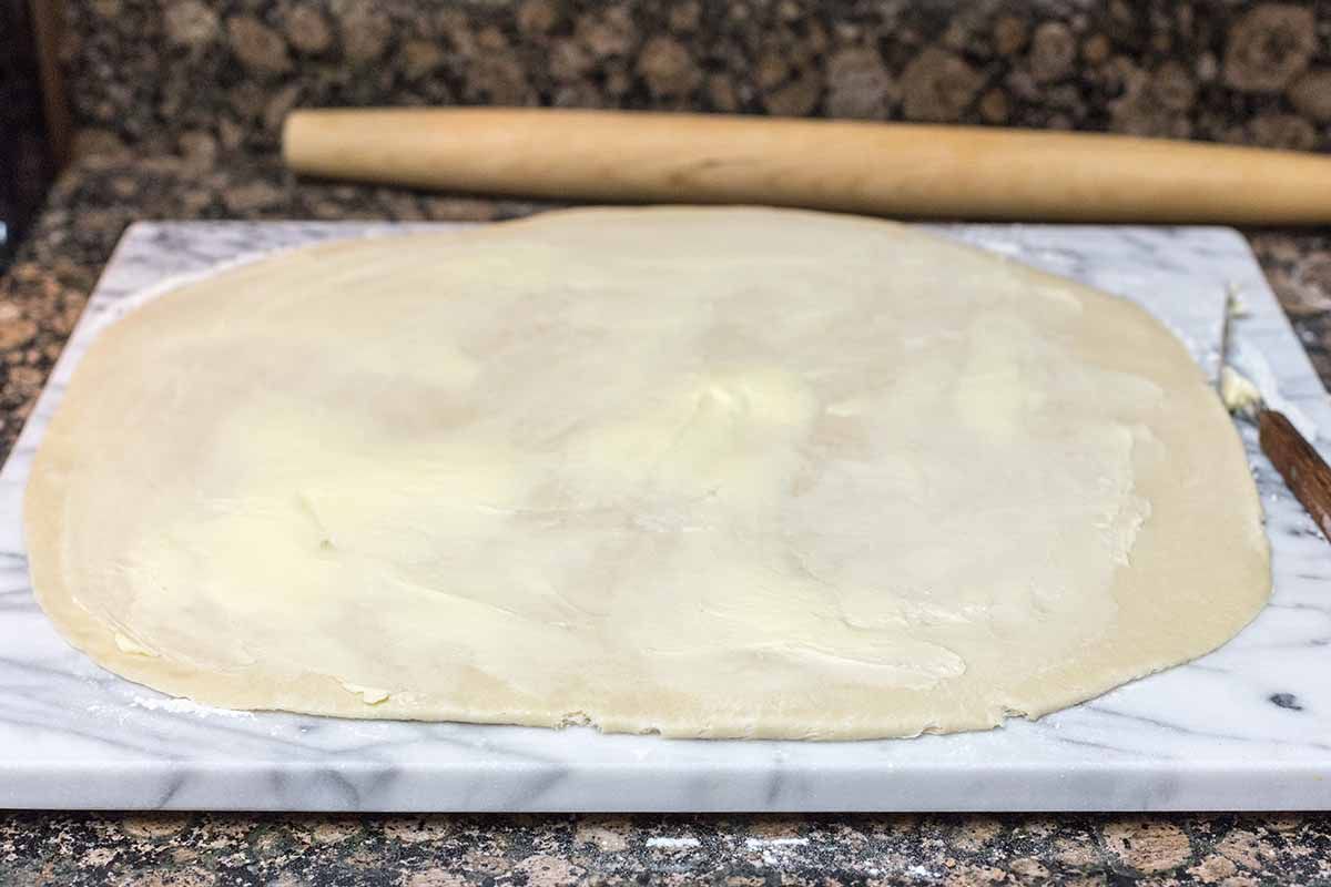 Dough for easy cinnamon rolls rolled out on a marble board with a rolling pin behind it.