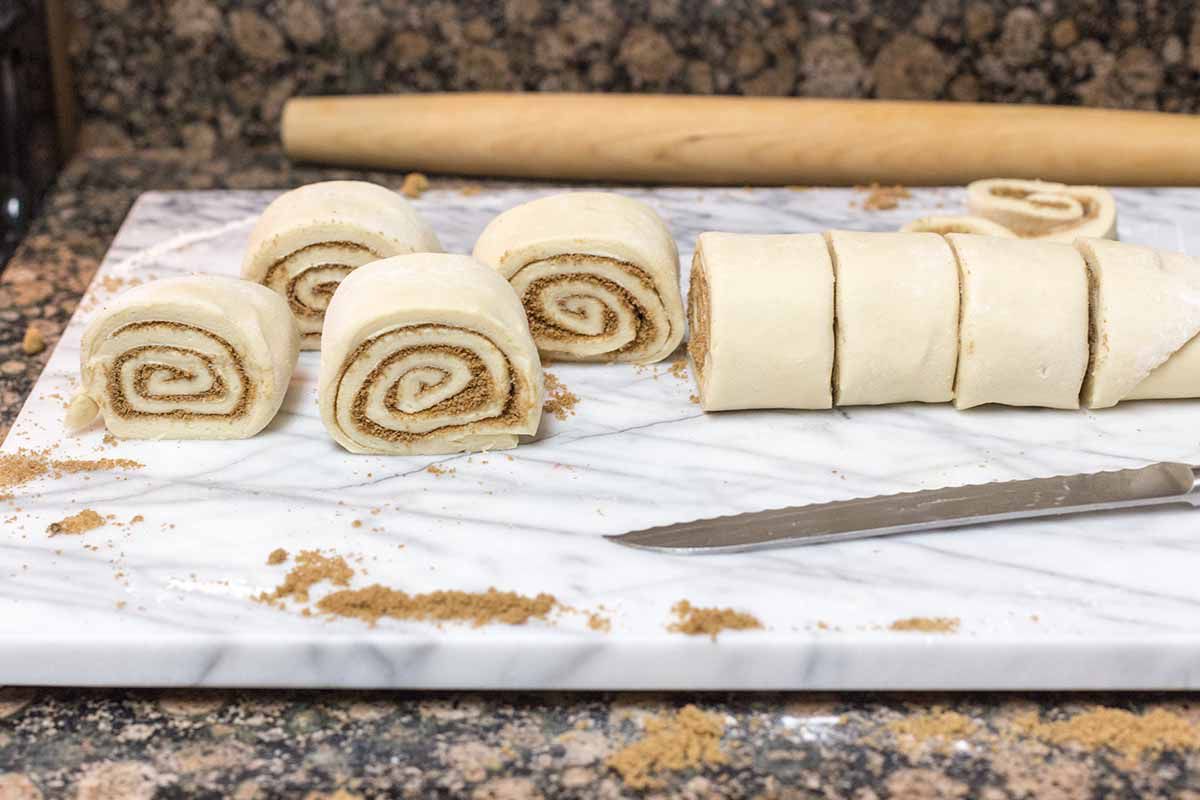 Cinnamon rolls from scratch cut into individual rolls with a bread knife. The inner spiral is visible and a rolling pin is behind them.