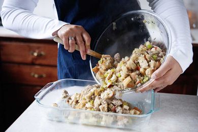 Woman in Blue Apron Spooning Stuffing from a Bowl to 9x13 Baking Dish 