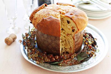 A loaf of homemade panettone in a paper mold with a slice cut out with a wreath around the base.