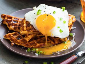 Sweet potato waffles on a plate, topped with a sunny side up egg and chives