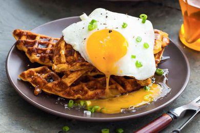 Sweet potato waffles on a plate, topped with a sunny side up egg and chives