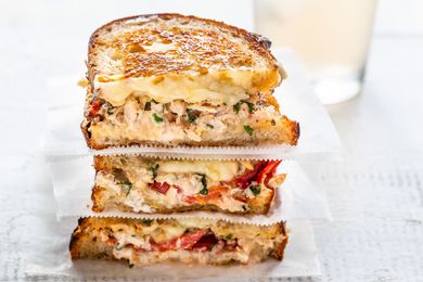 Grilled tuna sandwich cut in half and stacked on top of each other. The bread is toasted and tuna, melted cheese and tomatoes are visible in the filling.