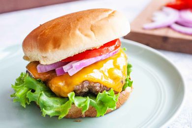 Grilled burger on a plate with cheese, onions, and tomatoes