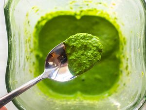 Top view of a spoon with kale pesto on it. The spoon is above a blender jar with more pesto inside.