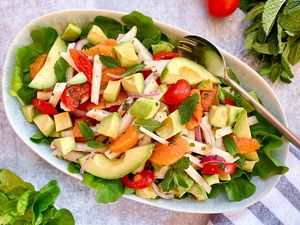 Overhead view of a summer citrus and avocado salad in a serving bowl. Mint and lettuce are also in the bowl.