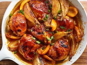 Harissa Honey Pargiyot in a white skillet on a wooden cutting board.