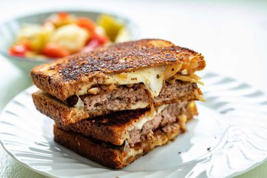 The best patty melt sliced in half and stacked on top of each other. The sandwich is crispy with melted cheese, caramelized onions and beef patties visible.