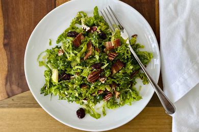 Raw Kale and Shaved Brussels Sprout Salad with Maple Dijon Vinaigrette on a plate with a fork to the right.