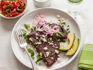 Mexican Enfrijoladas topped with avocado and cotija.