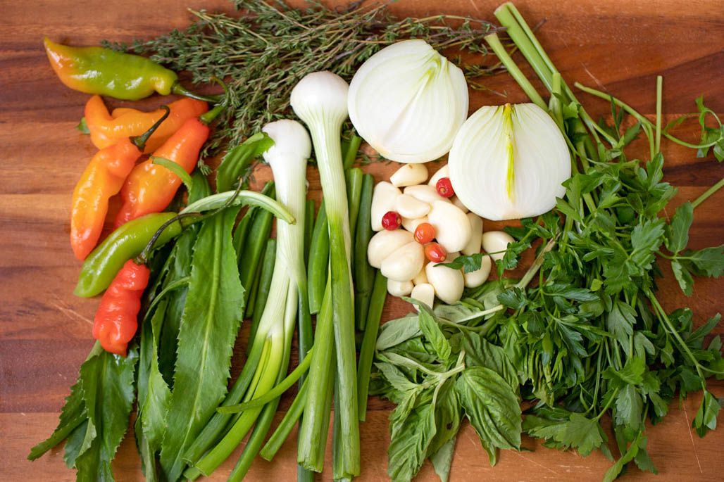 Carribbean green seasoning ingredients (L to R: peppers, culantro, thyme, green onions, halved white onion, garlic, basil, and parsely) 