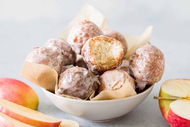 A bowl of cider glazed donut holes, one with a bite out of it, surrounded by red apples