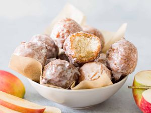A bowl of cider glazed donut holes, one with a bite out of it, surrounded by red apples
