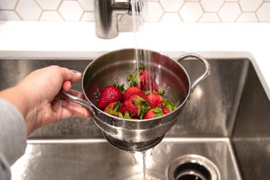 strawberries in colander under running water