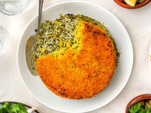 Sabzi Polo (Persian Herb Rice) on a Plate With a Serving Spoon, and Surrounding It, Small Plates With Sides and Glasses of Water 