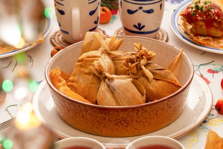 Tamales in a bowl at a table setting with plates, mugs, fresh fruit, and a tamale on a plate