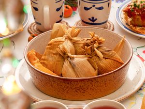 Tamales in a bowl at a table setting with plates, mugs, fresh fruit, and a tamale on a plate