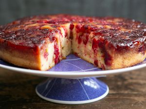 A cranberry upside-down cake on a platter with a slice cut out of it