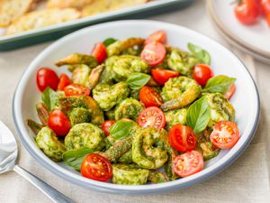 5-Ingredient Pesto Shrimp with Cherry Tomatoes in a Bowl, and in the Background, a Tray of Garlic Bread and Cherry Tomatoes