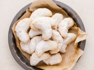 Overhead view of crescent cookies on parchment paper in a pan.