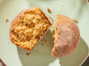 An apple cider donut muffin, broken in half and on a plate