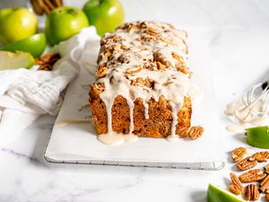 Apple Fritter Bread on Parchment Paper Surrounded by Granny Smith Apples, Pecans, and Sticks of Cinnamon