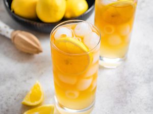 Two Glasses of Arnold Palmer With a Lemon Slice, Next to a Bowl of Lemons, a Citrus Reamer, and Lemon Wedges