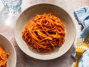 Bowlful of assassin's spaghetti at a table setting with more in a bowl, a glass of water, utensils, and light blue kitchen towel