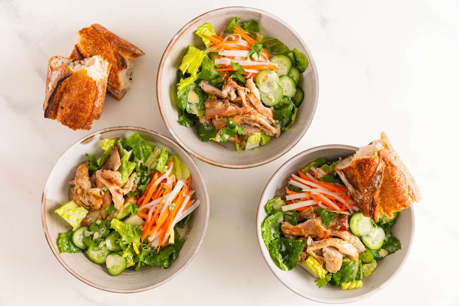 Three bowls of banh mi salad with chicken and doa chua, and served with slices of baguette