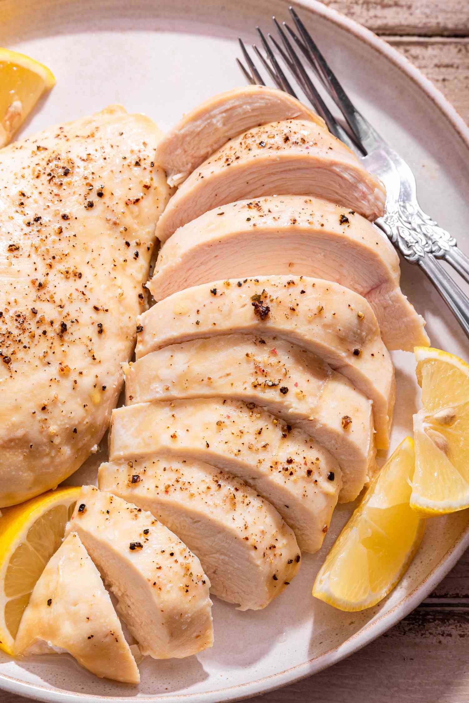 Close-up: chicken breasts (one cut into slices) on a plate with lemon wedges and utensils