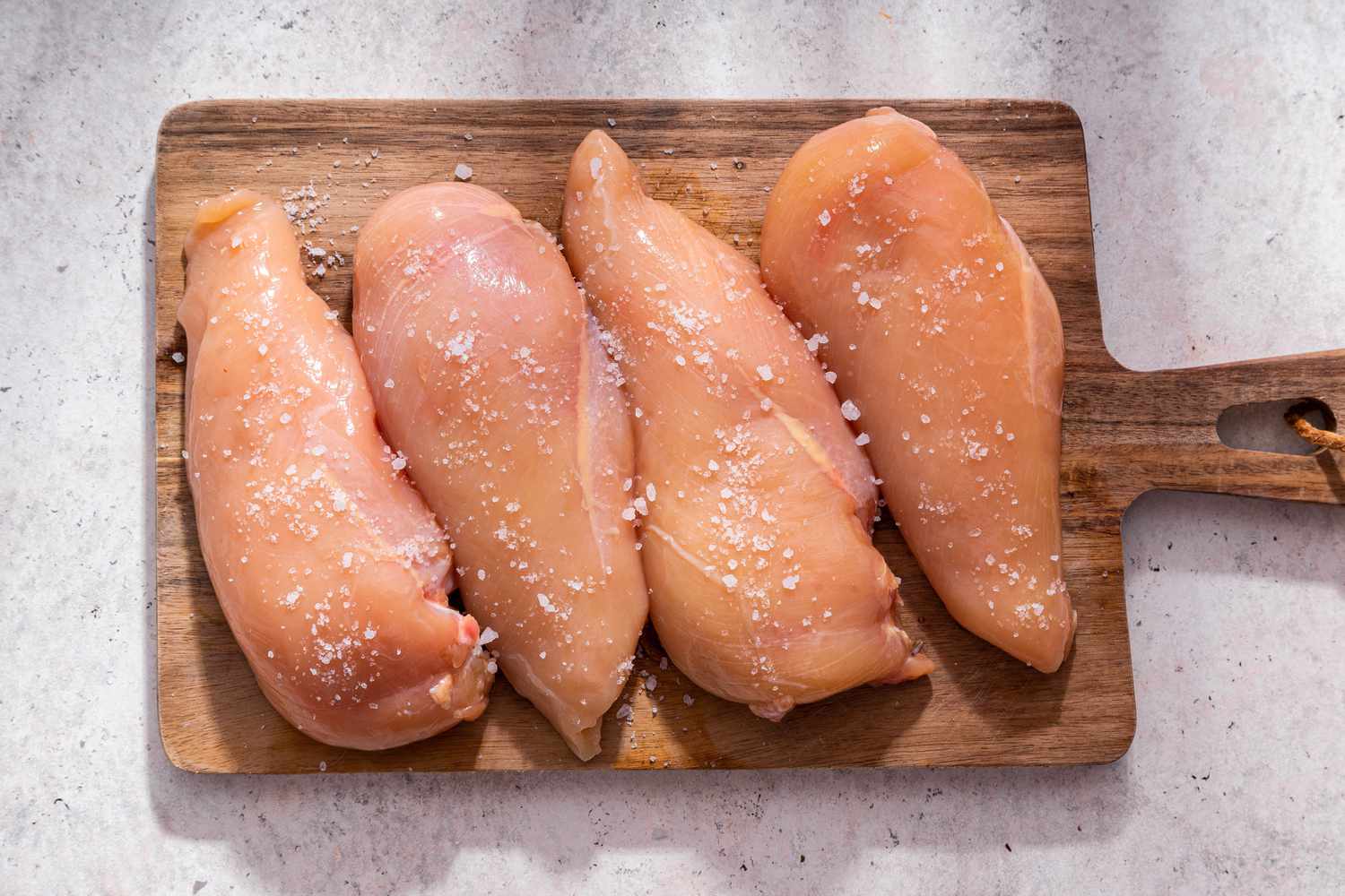 Salted chicken breasts on a cutting board for juicy baked chicken breast recipe