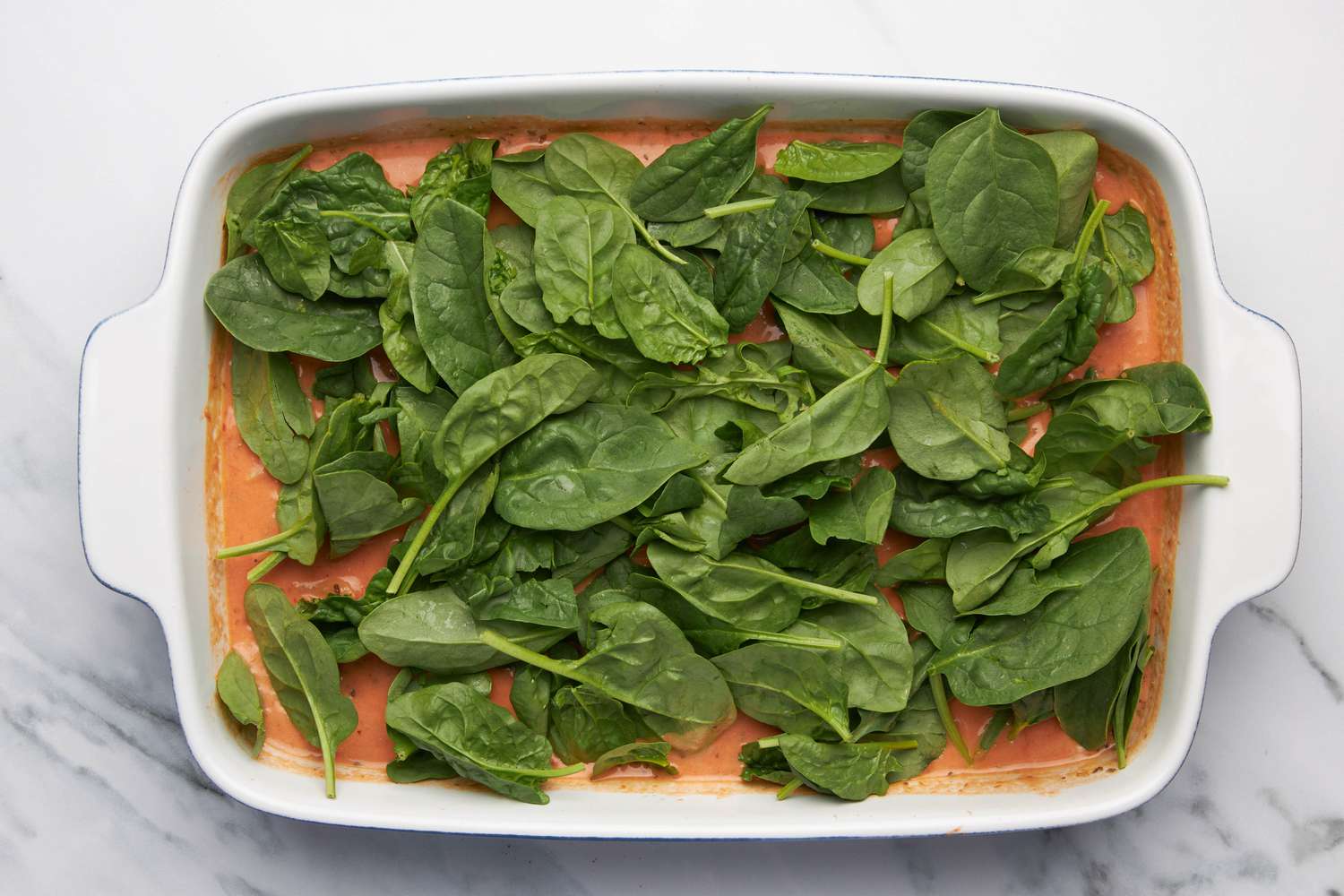 Casserole dish topped with fresh spinach for one pan baked penne alla vodka recipe