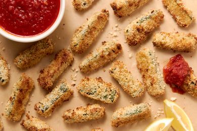 Baked Zucchini Fries on the Counter (One Was Dipped in Marinara Sauce), a Bowl of Marinara Sauce, and Lemon Wedges