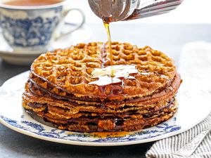 Pouring syrup over a stack of almond flour pancakes topped with butter
