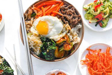 Bowl of Bibimbap Surrounded by Small Plates of Banchan (Side Dishes) and a Bowl of Bibimbap Sauce