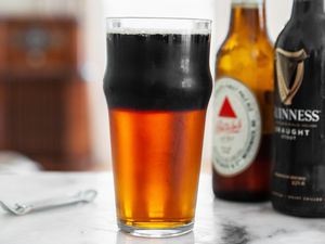 Glass of Black and Tan Next to Two Bottles of Beer and a Bottle Opener 