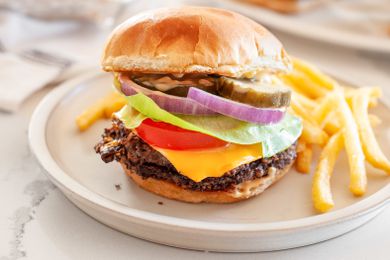 Black Bean Smash Burger on a Plate with French Fries, and in the Background, a Plate with More Burgers and a Tray with More Fries