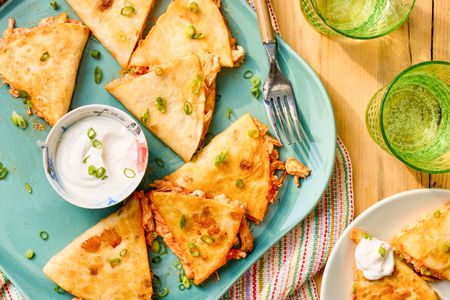 5-ingredient buffalo chicken quesadilla on a plate with a bowl of sour cream at a table setting with a serving on a plate, glasses of water, and a table runner