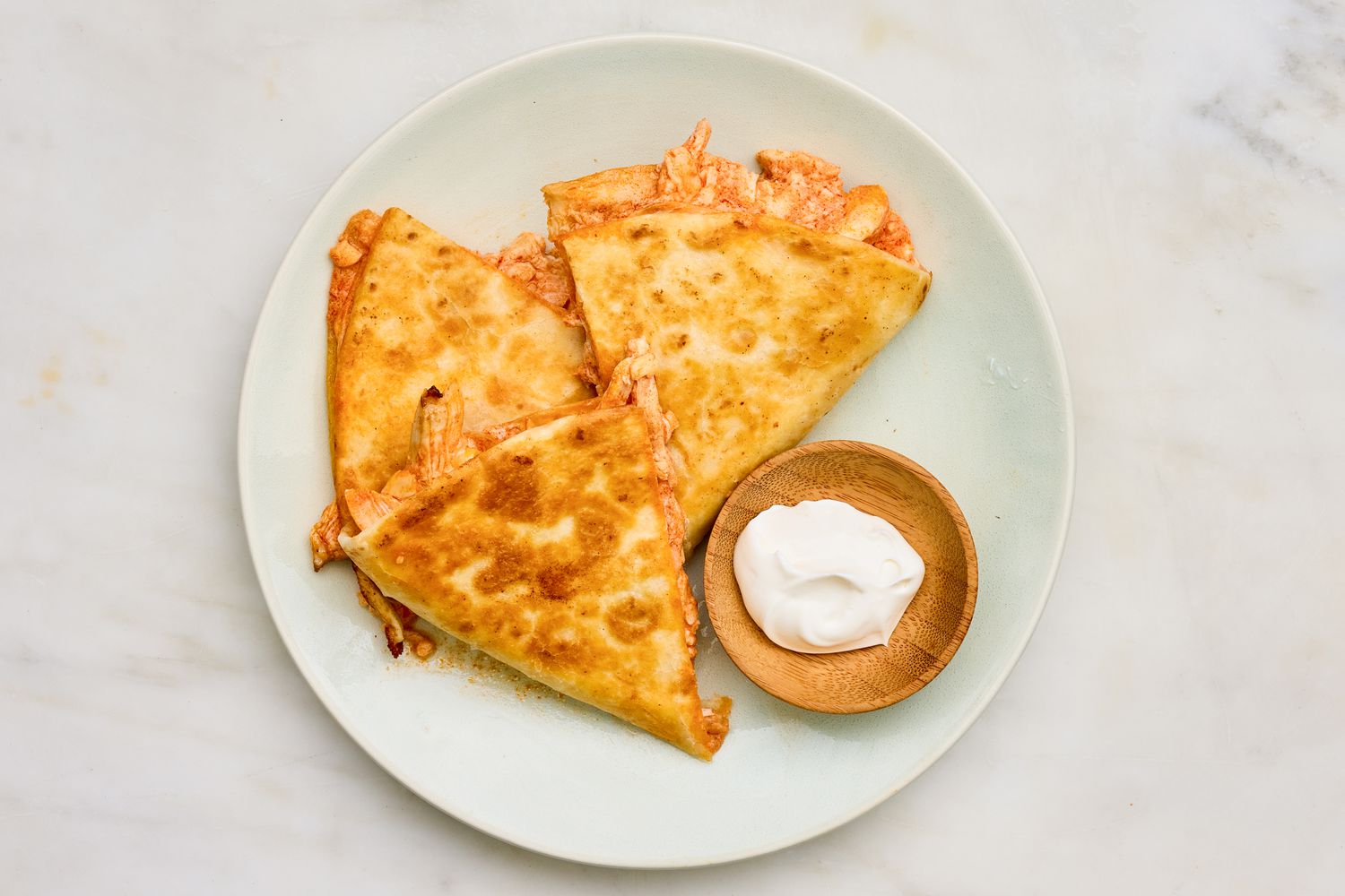 5-ingredient buffalo chicken quesadillas cut into slices and served on a plate with a bowl of sour cream