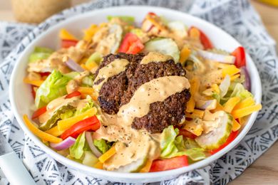 Bowl of Burger Salad Topped With a Hefty Drizzle of Dressing, Sitting on a Table Napkin