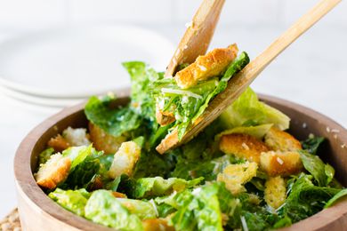 Serving Utensils Picking up Some Classic Caesar Salad Topped with Homemade Croutons