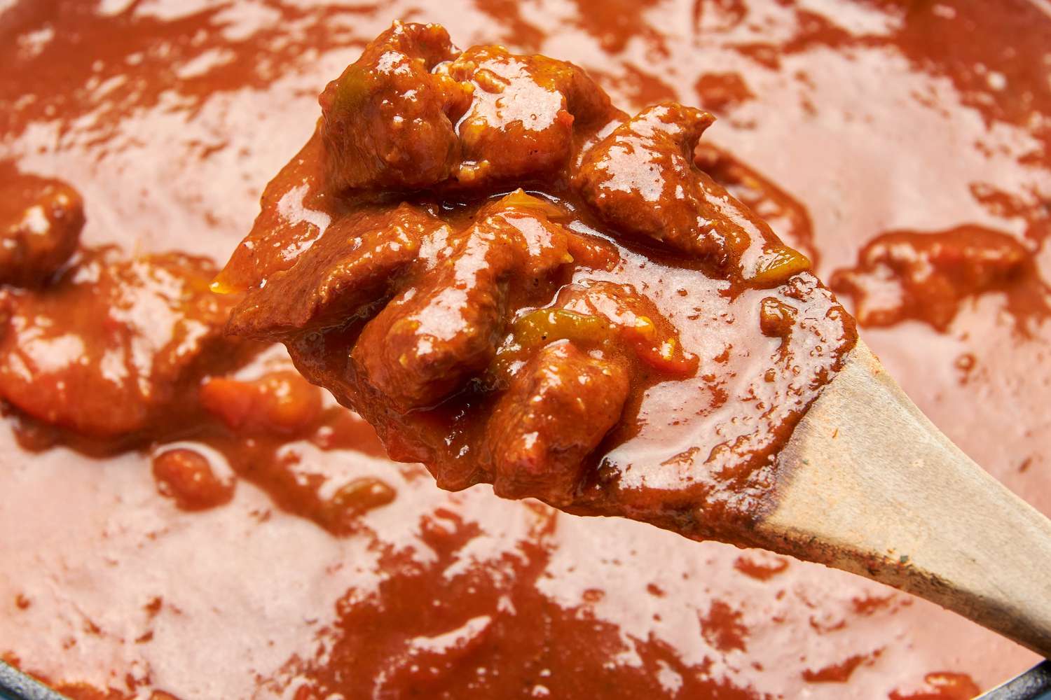 Pieces of carne picada lifted from Dutch oven using a wooden spoon