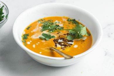 A bowl of blended coconut and carrot soup with savory cumin oil on a white background.