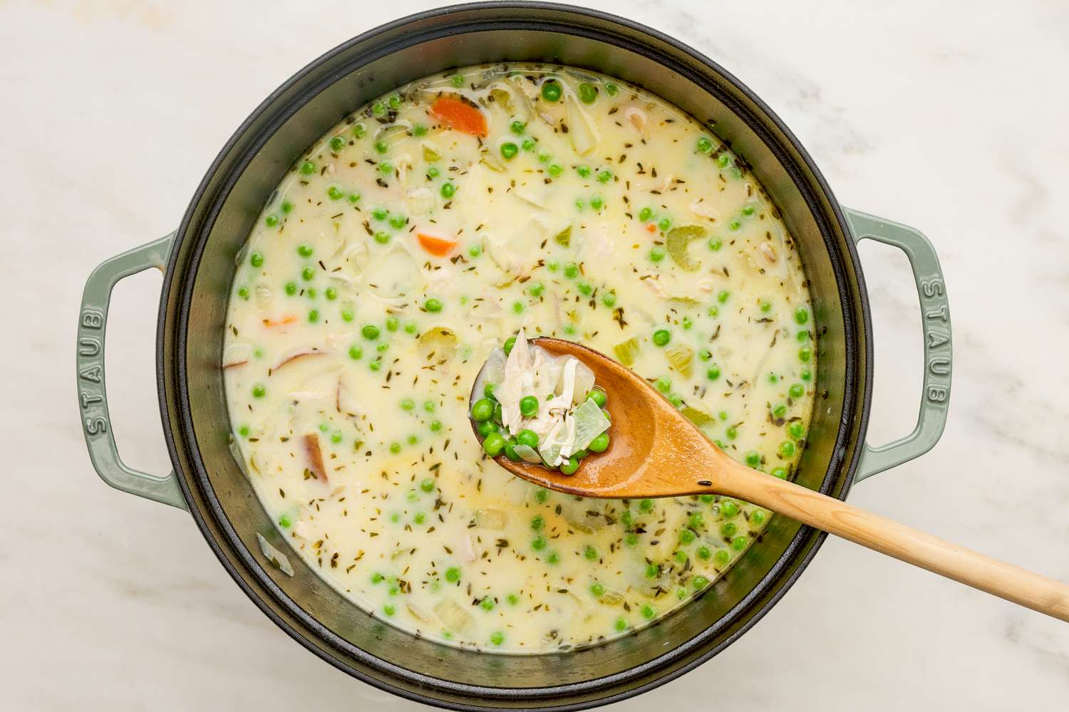 Half-and-half and frozen peas to the pot of chicken pot pie soup and some lifted on the wooden spoon