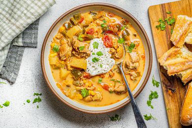 Bowl of Chipotle Chicken Chowder Next to a Wooden Board with Baguette Pieces and Table Napkin