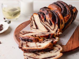 Semi-sweet chocolate babka on a wooden serving platter and three slices cut and laid in front.
