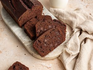 On a Marble Slab, Slices of Chocolate Banana Bread Next to the Rest of the Loaf, and on the Counter, a Glass of Milk, a Kitchen Towel, and a Slice of Bread