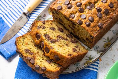 Platter of Chocolate Chip Zucchini Bread With Slices Cut Out and Cascading onto the Platter With a Kitchen Towel Underneath