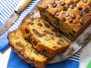 Platter of Chocolate Chip Zucchini Bread With Slices Cut Out and Cascading onto the Platter With a Kitchen Towel Underneath