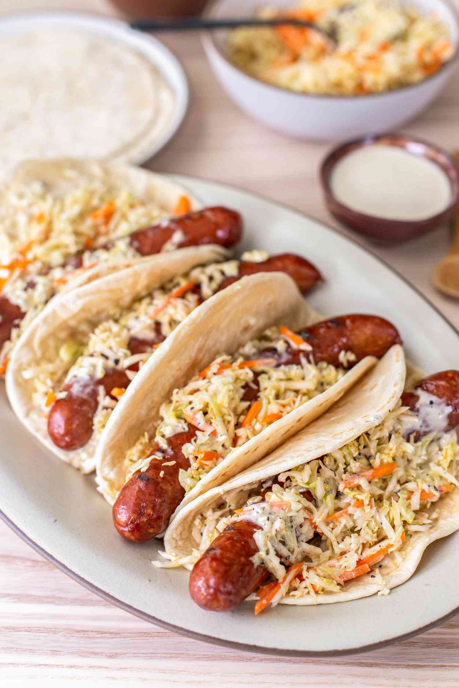 Plate of Ronto Wraps Topped With Slaw and Dressing, and in the Background, a Bowl of Coleslaw, a Plate With Pita Bread, and a Bowl of Dressing